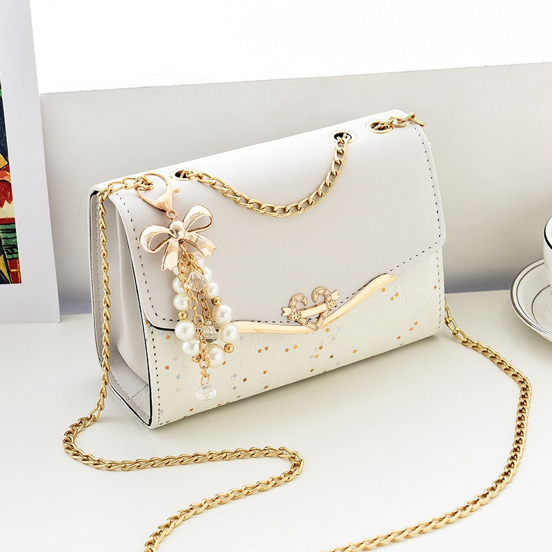 Sac cérémonie blanc à chaîne dorée, charm perlé et finition pailletée, format 21x14x8 cm, posé sur fond blanc