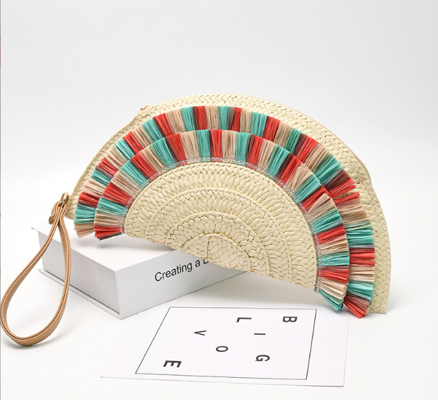 Pochette d’été rétro en paille naturelle, forme demi-lune, avec détails colorés corail et turquoise, format 33x16,5 cm, portée à la main
