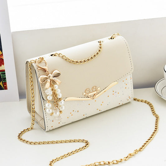 Sac cérémonie blanc à chaîne dorée, charm perlé et finition pailletée, format 21x14x8 cm, posé sur fond blanc

