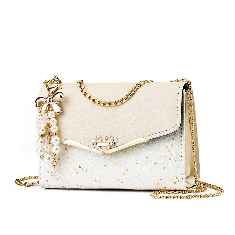 Sac cérémonie blanc à chaîne dorée, charm perlé et finition pailletée, format 21x14x8 cm, posé sur fond blanc

